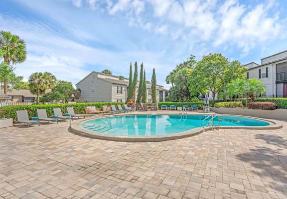 A swimming pool surrounded by a brick patio and lounge chairs.