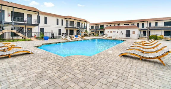 A pool surrounded by sun loungers in front of apartment buildings.