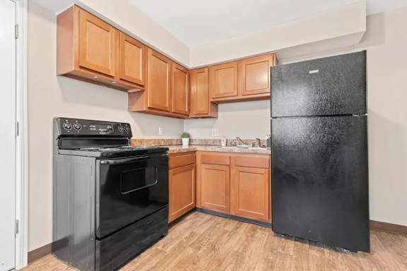 A black fridge sits in a kitchen with wooden cabinets.