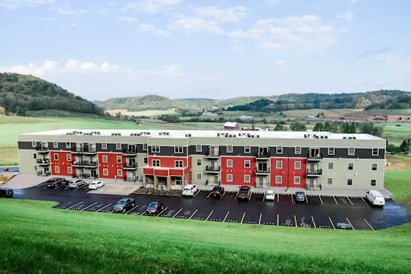 A large building with red and white sections is surrounded by a parking lot.