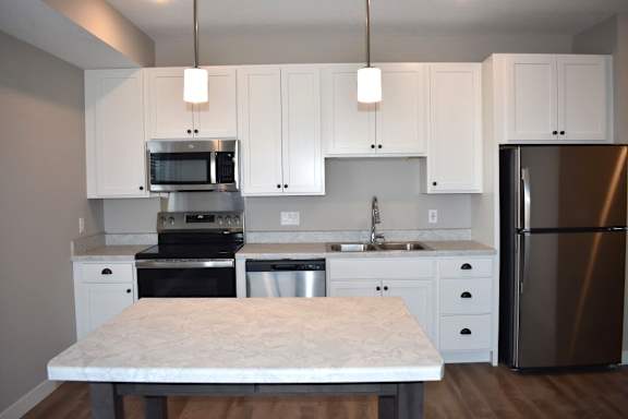 A kitchen with a table in the middle and a refrigerator on the right.
