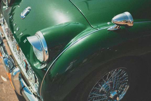 A green vintage car is parked with its side facing the camera.