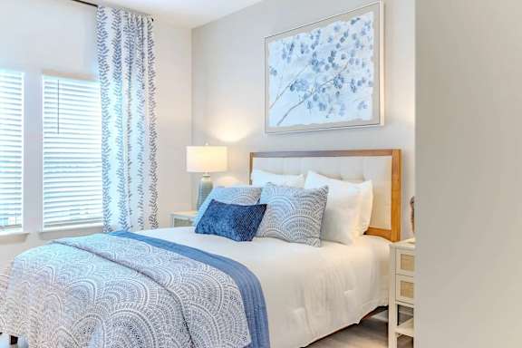 A bedroom with a bed, chair, and artwork on the wall.