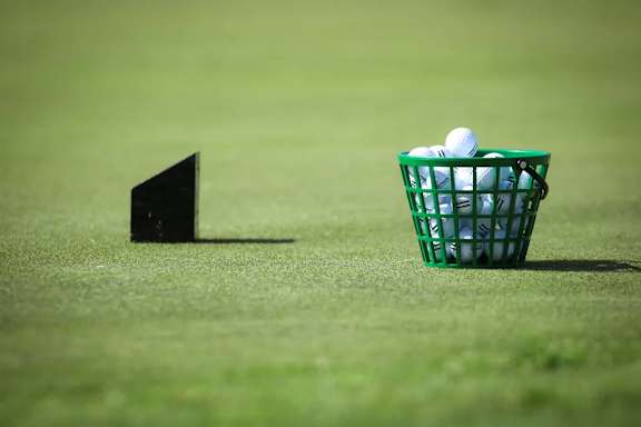 A green basket with golf balls in it is on a green field.