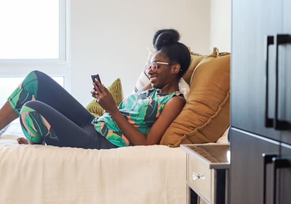 a woman laying on a bed looking at her phone in her Citizen Studio Apartment  at The Citizen Birmingham