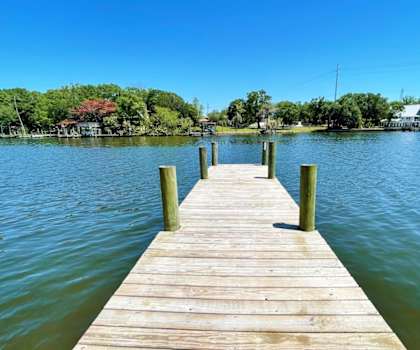 A wooden dock extends into a calm body of water with a clear blue sky above.