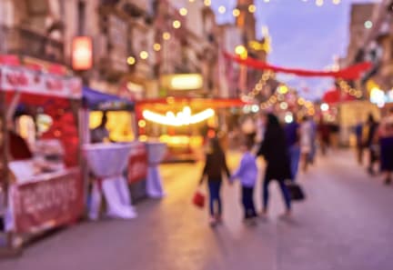 A blurry image of a street with people walking and stalls with red balloons.