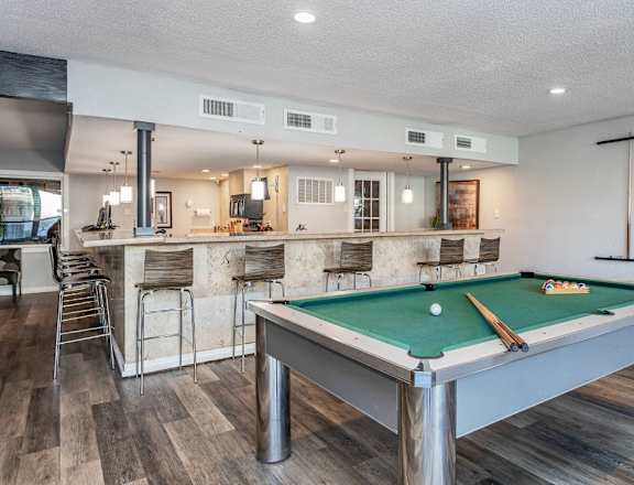A pool table is in the middle of a room with a bar area.