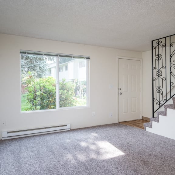 an empty living room with a staircase and a large window
