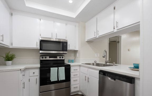 a kitchen with white cabinets and black appliances and a sink at Huntington Terrace North Senior, California, 92648
