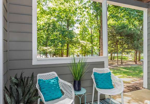 Two white chairs with blue pillows sit on a porch.