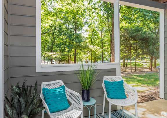 Two white chairs with blue pillows sit on a porch.