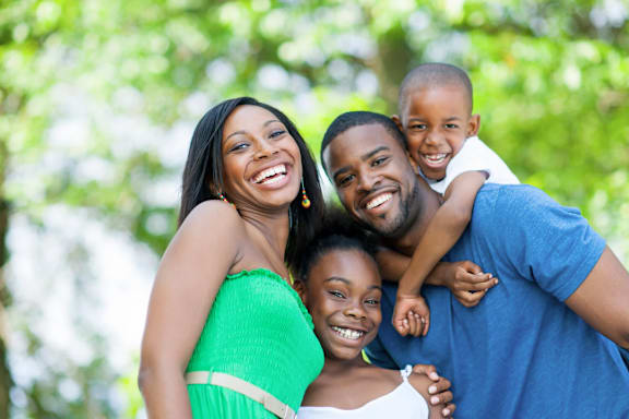 A family of four is smiling and enjoying their time together in a park.