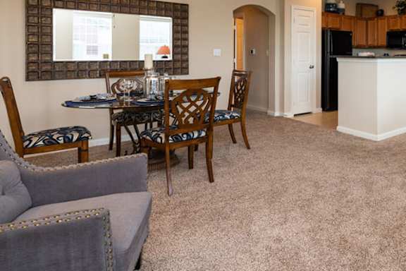 a living room with a couch a table and chairs and a kitchen in the background