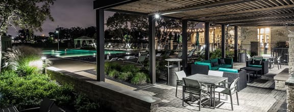 a patio with tables and chairs and a pool at night