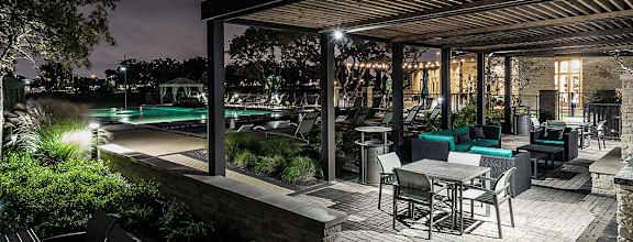 A patio with a table and chairs overlooking a pool at night.