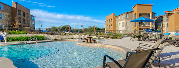 A swimming pool surrounded by lounge chairs and umbrellas in a sunny day.