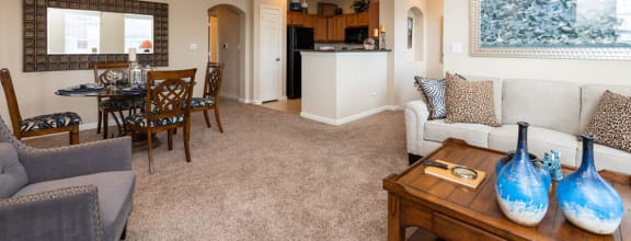 a living room with a couch a table and chairs and a kitchen in the background