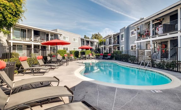 a swimming pool with chairs and umbrellas in front of an apartment building