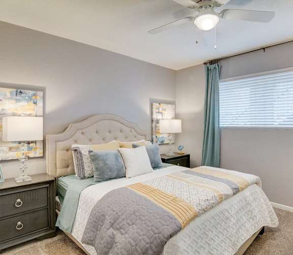 A bedroom with a large bed, two nightstands, and a ceiling fan.