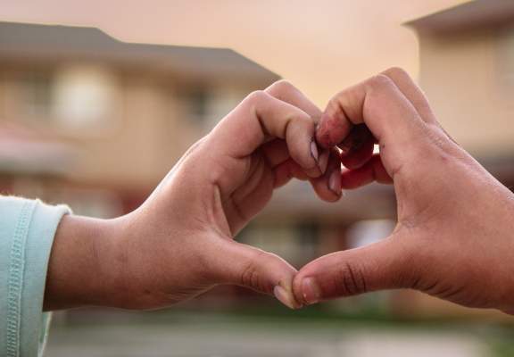 Two hands forming a heart shape against a blurred background.