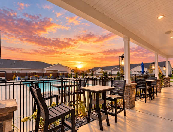 A sunset view from a covered patio with chairs and tables.