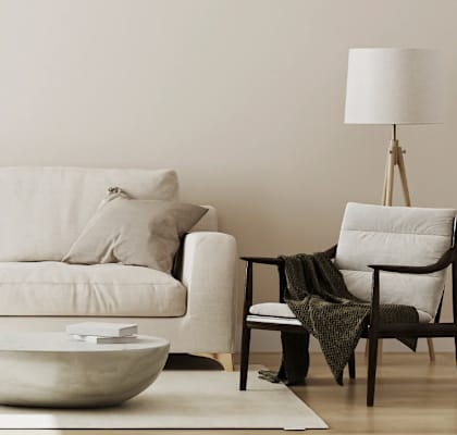 A white couch with a bowl on the floor and a chair with a blanket on it.