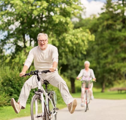 An elderly man rides a bicycle in a park.