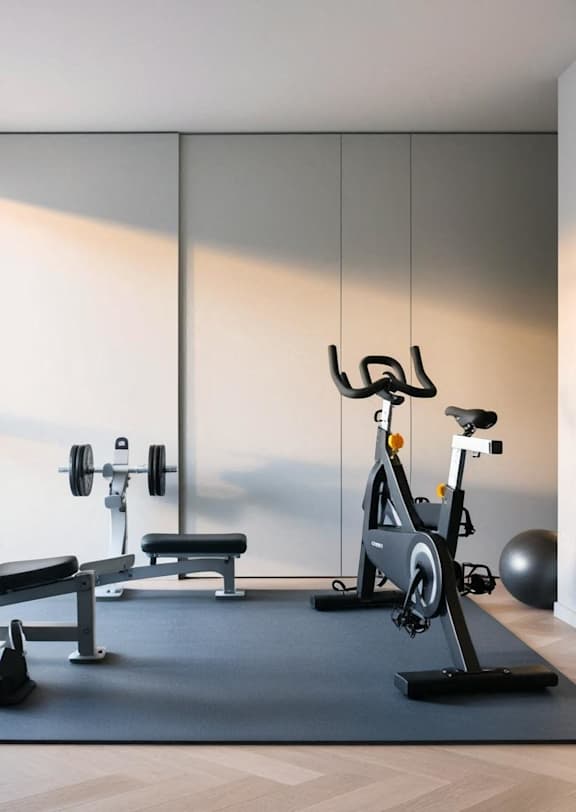 A modern home gym with a stationary bike, a bench, and dumbbells.
