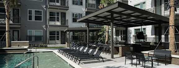 A pool area with lounge chairs and a barbecue grill.