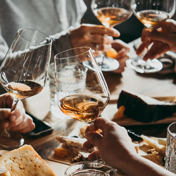 A group toasts with wine over a charcuterie board in a warm, elegant setting.