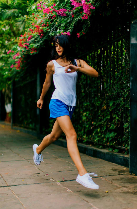 a woman in a white tank top and blue shorts running down a sidewalk