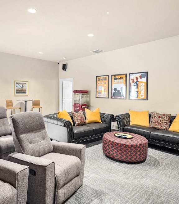 A living room with a grey chair and a black couch with yellow pillows.