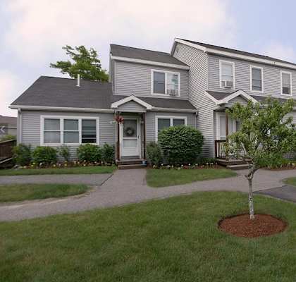 A grey house with a tree in front of it.