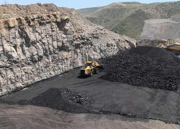 A large yellow bulldozer is moving a pile of black coal.