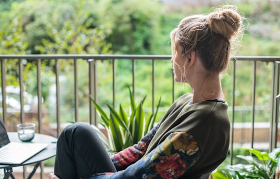 A woman is sitting on a balcony with a laptop on a table.