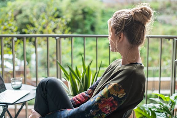 A woman is sitting on a balcony with a laptop on a table.