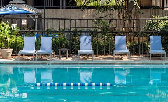 A pool with blue chairs and a black fence.