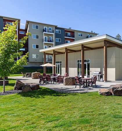 A modern building with a glass facade and a covered patio area with tables and chairs.