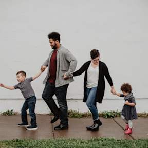 A family of four is walking together on a sidewalk.