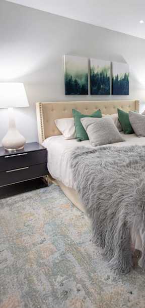 A bed with a grey furry blanket and green pillows.