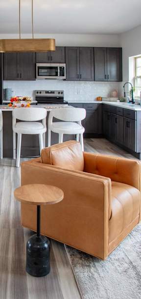 A brown leather chair with a wooden stool in front of a kitchen.