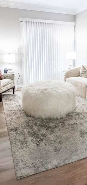 A white fluffy ottoman sits on a rug in a living room.