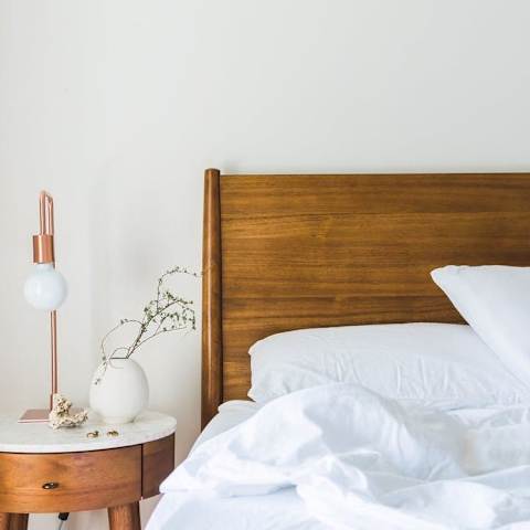 Model Bedroom with Wood Bed Frame and White Bedding Next to Wood Nightstand