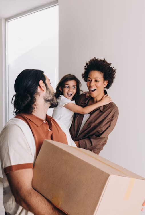 A man is carrying a box while two women embrace him.