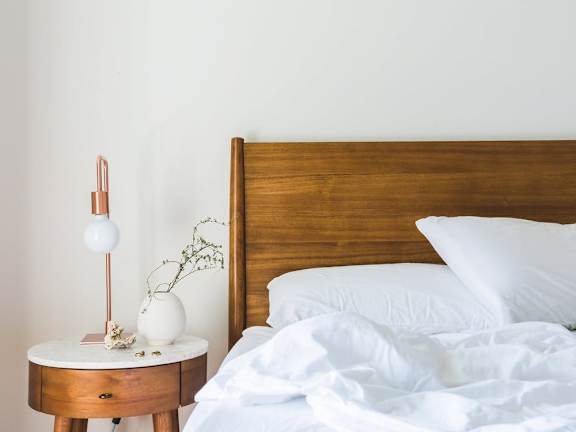 Model Bedroom with Wood Bed Frame and White Bedding Next to Wood Nightstand