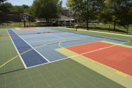 A gated multifunctional sports court at New Kent Apartments in West Chester, PA, featuring a basketball hoop, tennis net, and surrounded by lush grass and trees