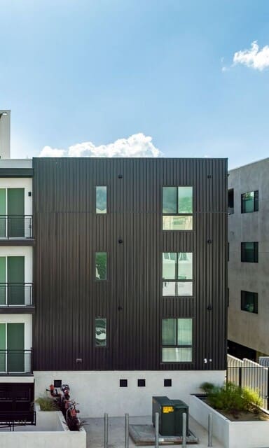 A modern building with a black facade and two cars parked in front.