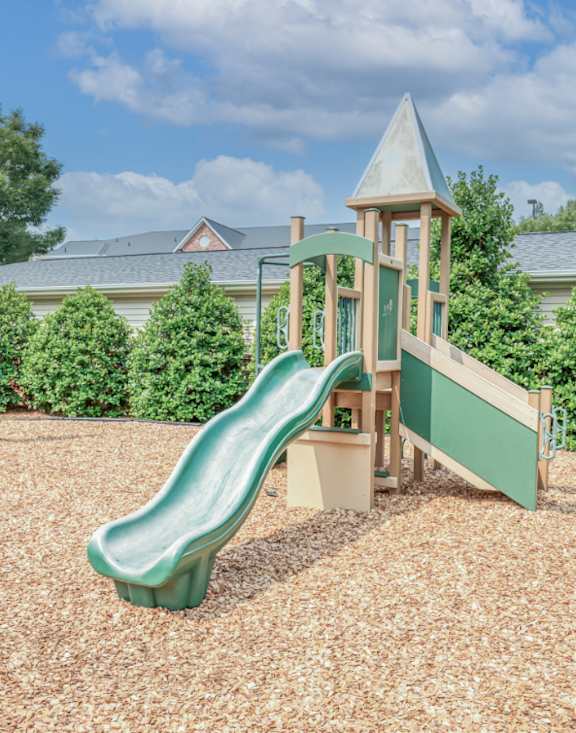 A playground with a green slide and a wooden structure.