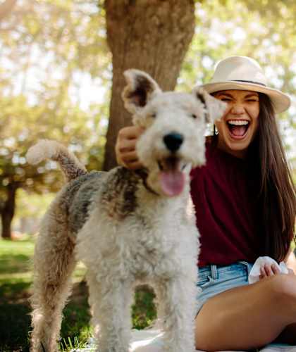A woman and a man are sitting on a blanket with a dog in a park.